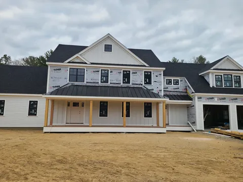 Before: April 24, 2022: house wrap and windows in. October 2023: the same farmhouse finished, with its porch, siding and landscaping.